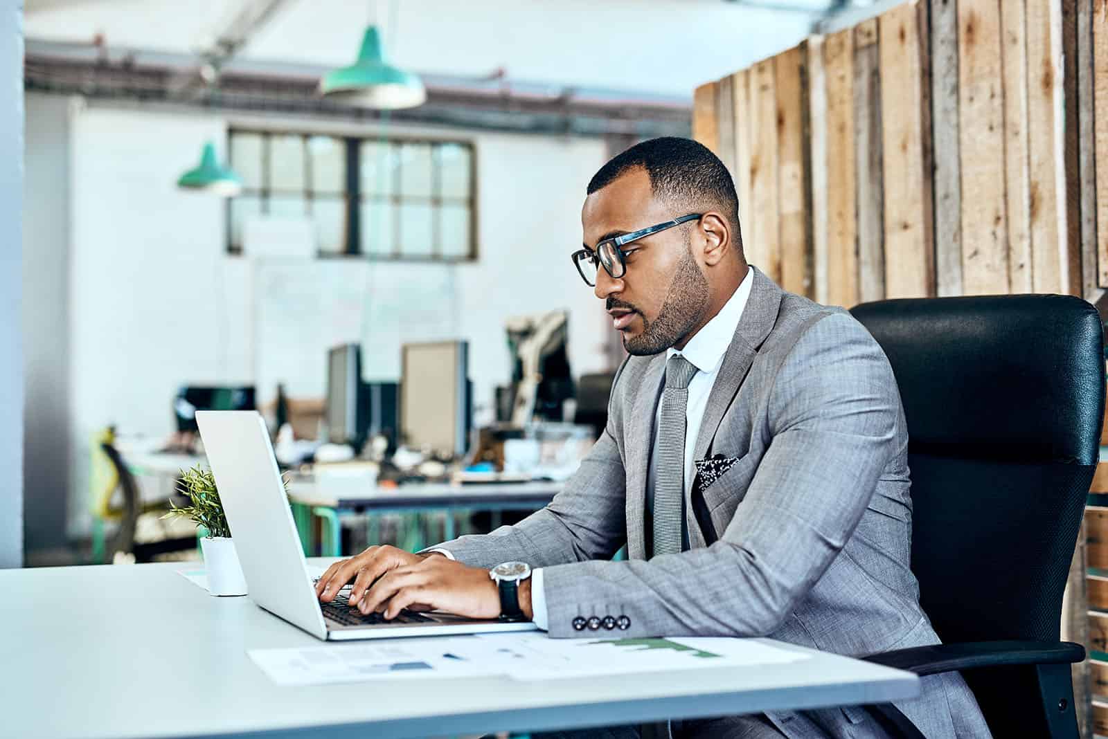 Man in glasses sitting at a desk working on his laptop